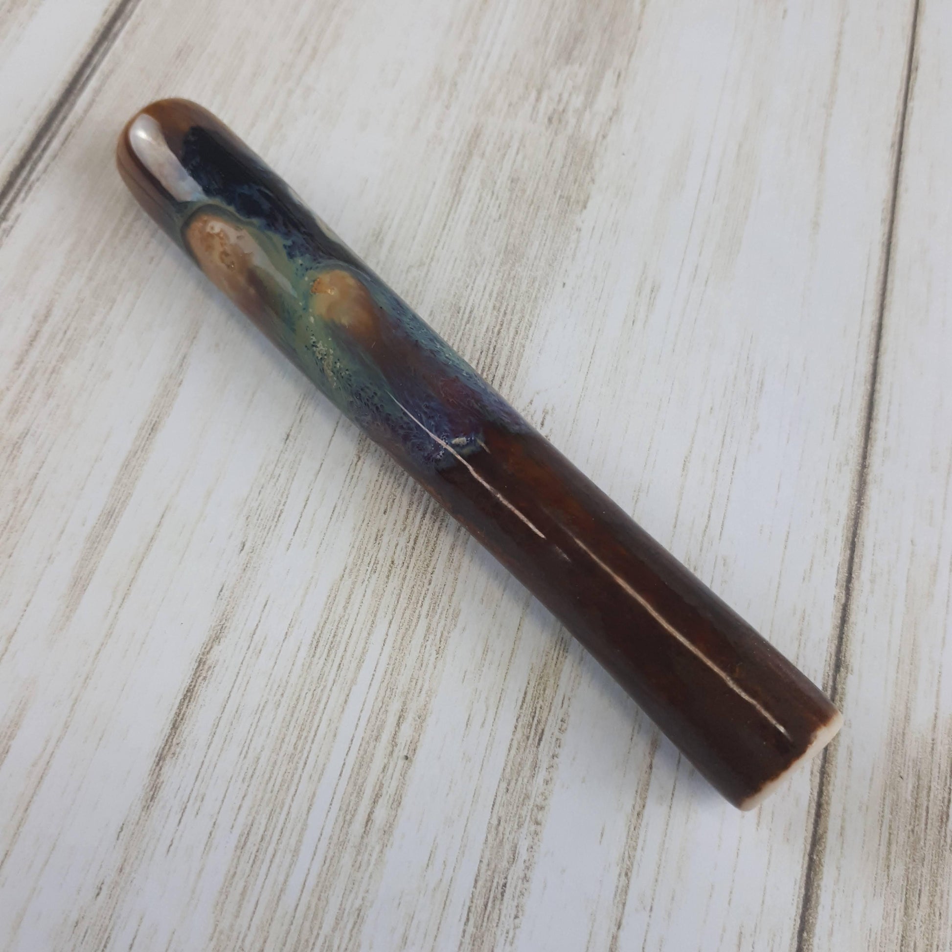 Dirty Peacock uno chillum pipe side view. brown, with blue/green drips and white bursts