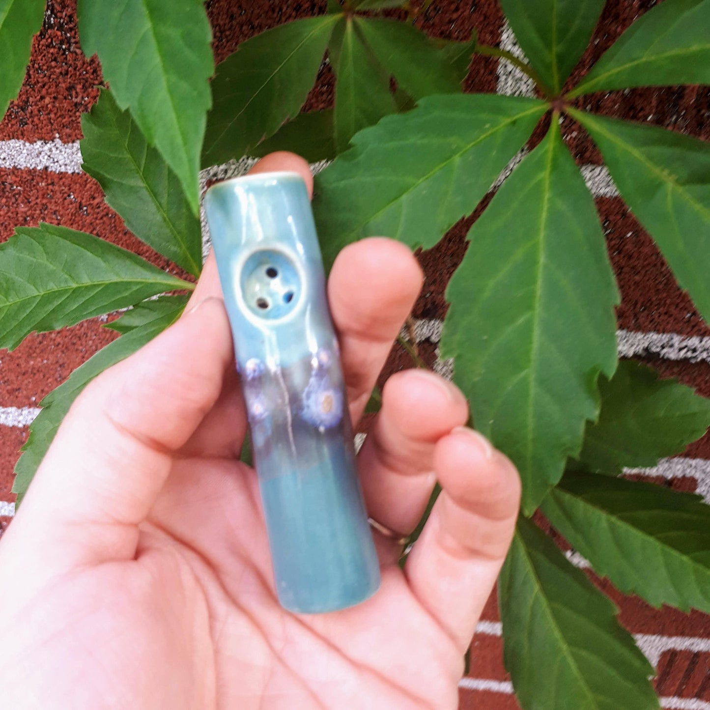 Blue Dream mini purse pipe held in hand against brick wall covered in leaves